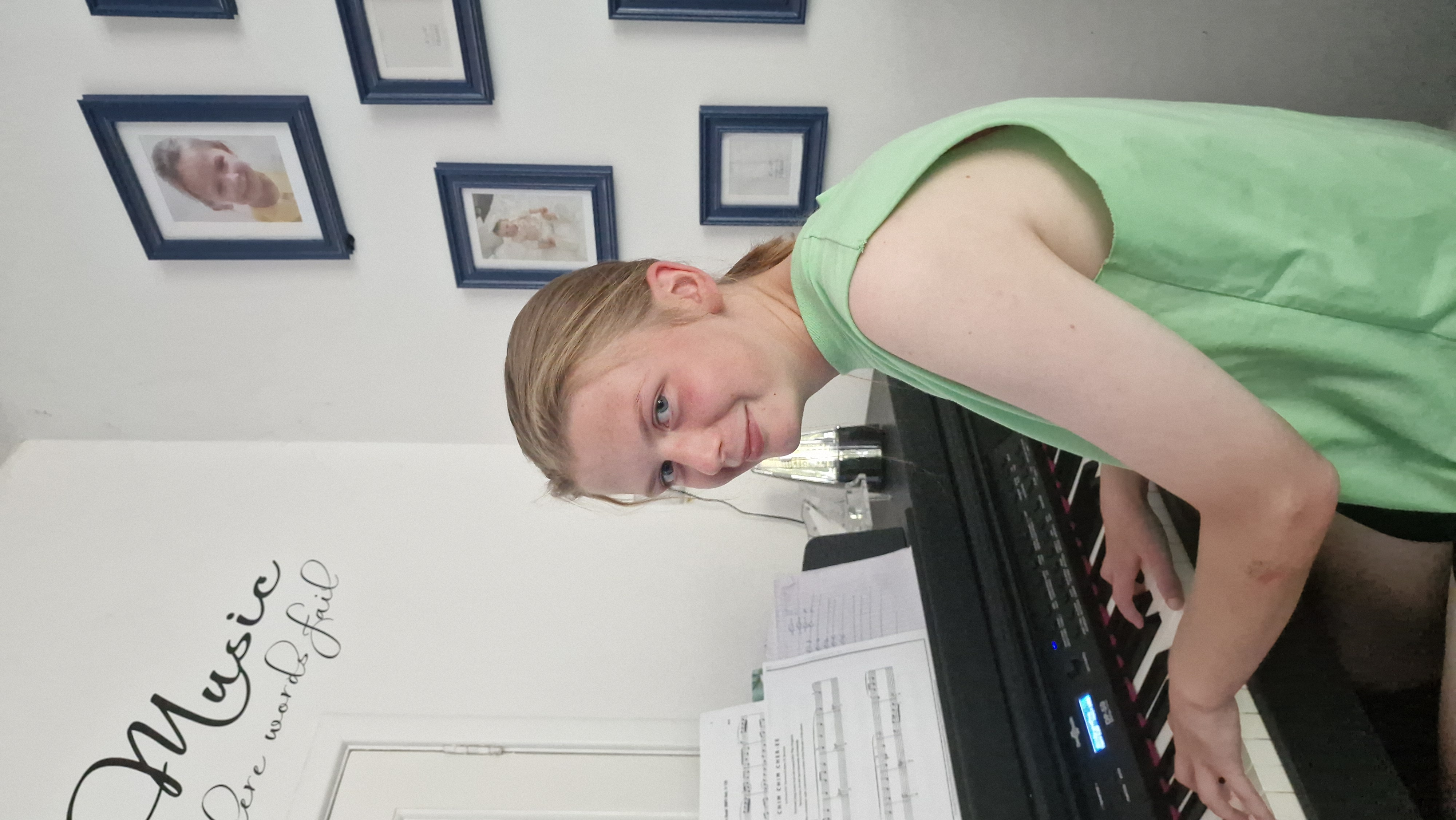 A young piano pupil learning at her digital keyboard at home, with sheet music in front of her